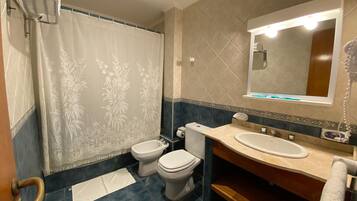 Un baño con cortina de ducha, dos inodoros, un lavabo, un espejo y un perchero para toallas.