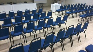 Uma sala de conferências com fileiras de cadeiras azuis, uma tela de projeção e um quadro branco.