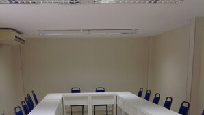Uma sala de conferência com uma mesa comprida, cadeiras azuis e um projetor sobre a mesa.