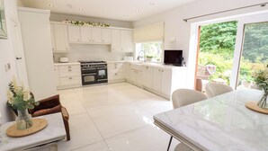 A modern kitchen with white cabinets, a black stove, and a dining area with a marble table. - St Mary's House (Oldham)