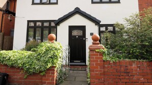 A two-story house with a black front door, a small porch, and a number '12' on the wall. - St Mary's House (Oldham)