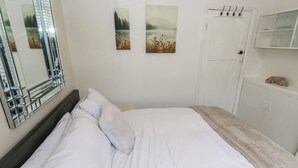 A bedroom with a large bed, white bedding, a mirror, and a door with a towel rack. - St Mary's House (Oldham)
