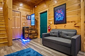 A cozy room with wooden walls, a grey sofa, a blue rug, and a neon sign that says 'LET'S PLAY'. - 84° Heated Indoor Pool, Hot Tub, Game Room, Views (Sevierville)