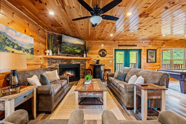 A cozy cabin interior with a fireplace, two sofas, a coffee table, and a ceiling fan.
