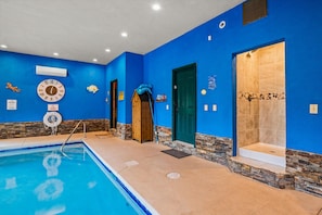 A swimming pool with a blue interior, a wooden deck, and a stone wall.