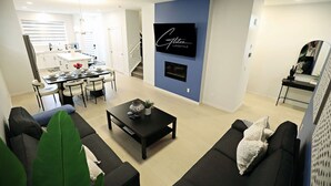 En moderne stue med en sort sofa, et sofabord og en pejs. Der er et spiseområde med et bord og stole.