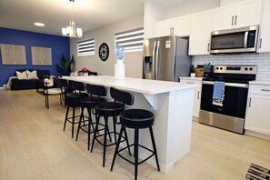 Una cuina moderna amb una illa central, tamboretes de bar, electrodomèstics d'acer inoxidable i una paret d'accent blava.