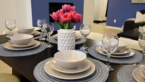 Et spisebord dækket med hvide tallerkener, skåle og glas, med en vase med lyserøde blomster i midten.