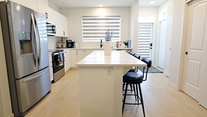 Et moderne køkken med rustfrie hvidevarer, en central ø med barstole og et stort vindue med persienner.