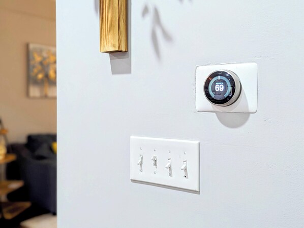 A thermostat and a set of light switches on a wall.