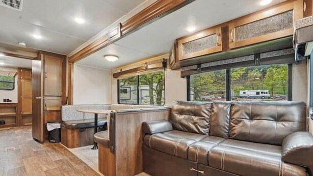 Un interior de autocaravana espacioso con sofá de cuero, mesa de comedor y zona de cocina.