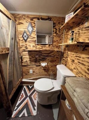 Une petite salle de bain au style rustique, avec un intérieur en bois, des toilettes blanches, un petit miroir et un espace douche.