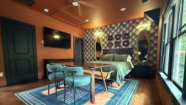 Een slaapkamer met een bed, een bureau, twee stoelen, een televisie en een groot raam.