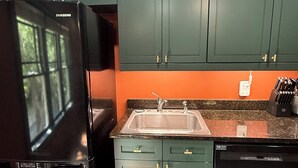 Een keuken met groene kastjes, een zwarte koelkast en een vaatwasser.