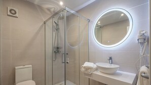 A modern bathroom with a glass-enclosed shower, a round mirror, a sink with a bowl, and a toilet.