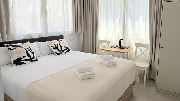 A hotel room with a large bed, a small table with a coffee maker, and a wardrobe.