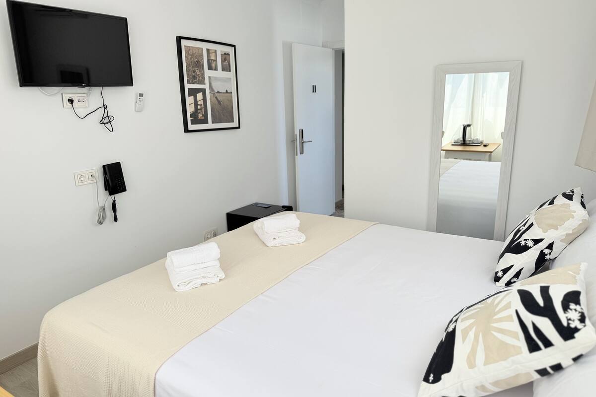 A hotel room with a bed, a flat-screen TV mounted on the wall, a telephone, and a framed photo.