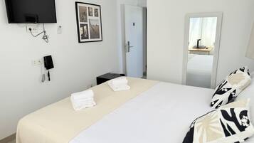 Habitación de hotel con cama, televisor de pantalla plana montado en la pared, teléfono y una fotografía enmarcada.