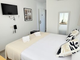 A hotel room with a bed, a flat-screen TV mounted on the wall, a telephone, and a framed photo.