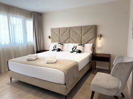 A modern hotel room with a large bed, a bedside table, a chair, and a window with curtains.