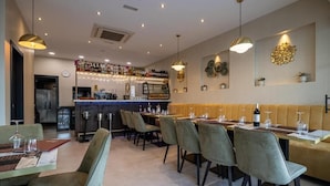 A restaurant with a bar area, seating for 10, and a counter with a wine display.