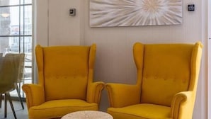 A room with two yellow armchairs, a small round table, a modern light fixture, and a large abstract painting on the wall.