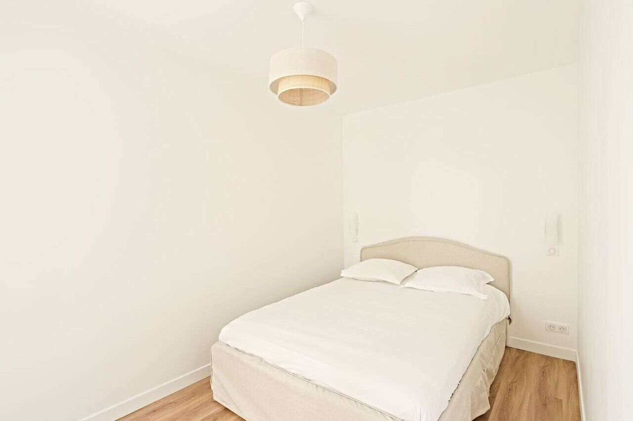 A minimalist bedroom with a single bed, a hanging light fixture, and a plain white wall.