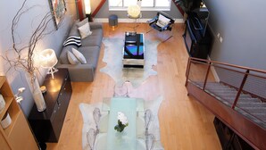 Un vaste espace de vie doté d’un haut plafond, d’une grande fenêtre, d’un canapé, d’une table basse et d’un escalier.
