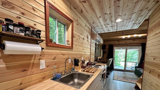A wooden cabin interior with a kitchen featuring a sink, countertop, and various kitchen items.