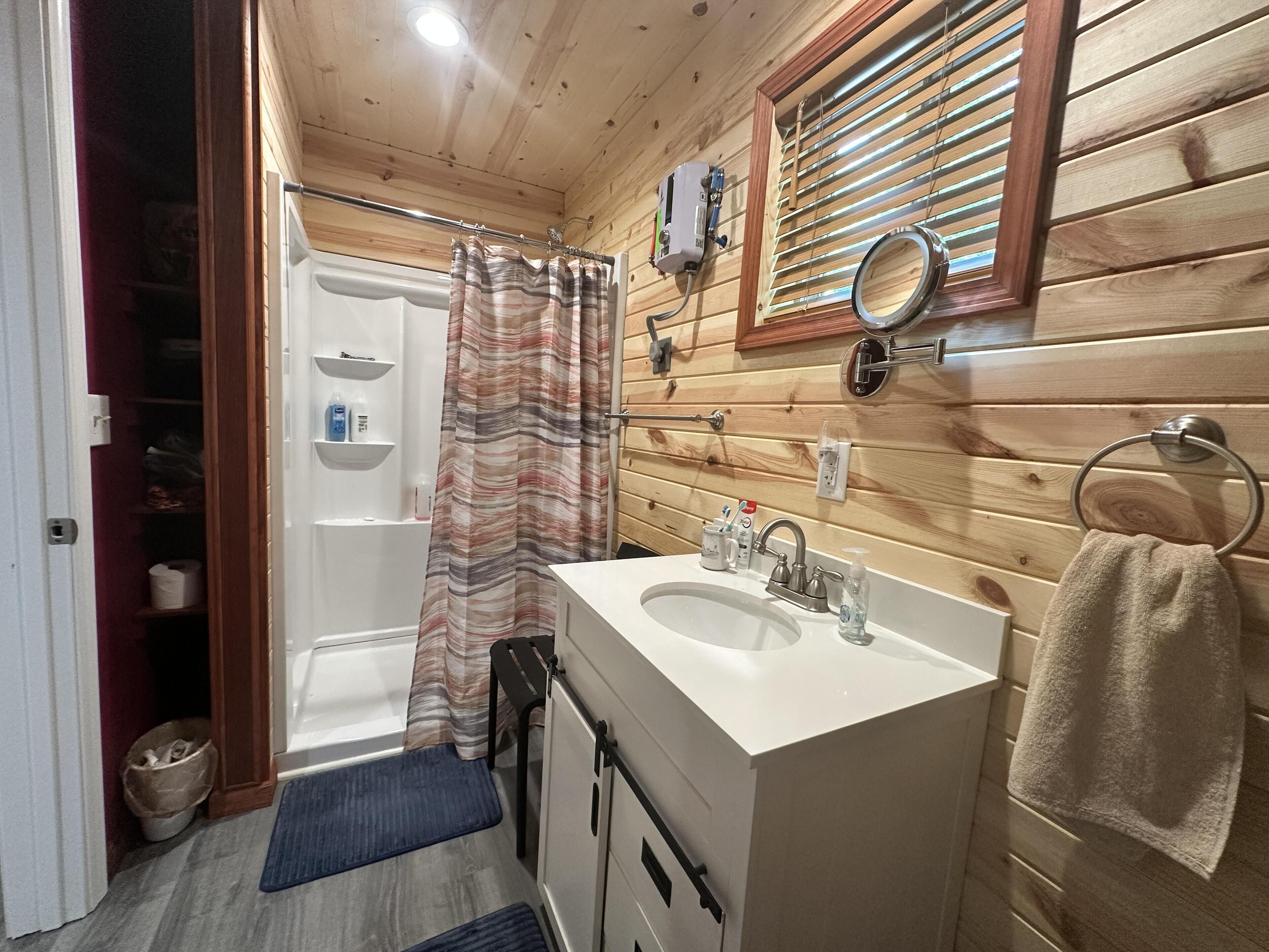 Une salle de bain aux murs lambrissés, équipée d’une douche, de deux lavabos, d’un miroir et d’un porte-serviettes.