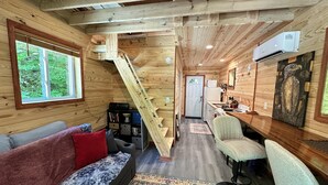 A cozy cabin interior with a wooden interior, a sofa, a chair, a small kitchen area, and a staircase.