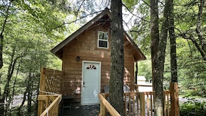 A wooden cabin with a white door, surrounded by trees, and accessible by a wooden staircase.