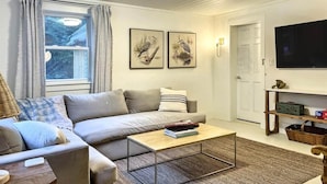 En stue med sofa, sofabord, fjernsyn og billeder på væggen.