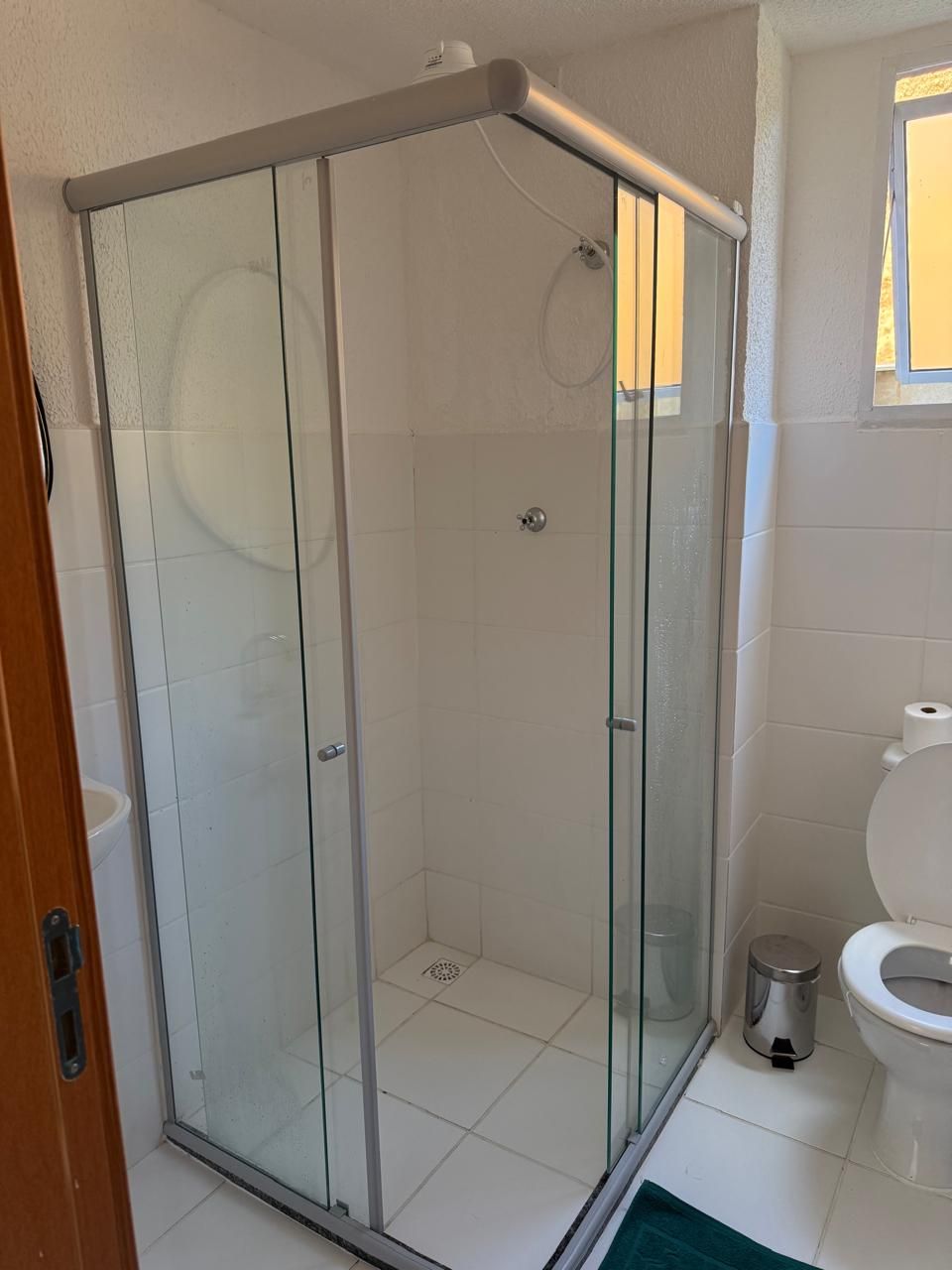 A glass-enclosed shower with a metal frame, a toilet, and a trash can in a bathroom.