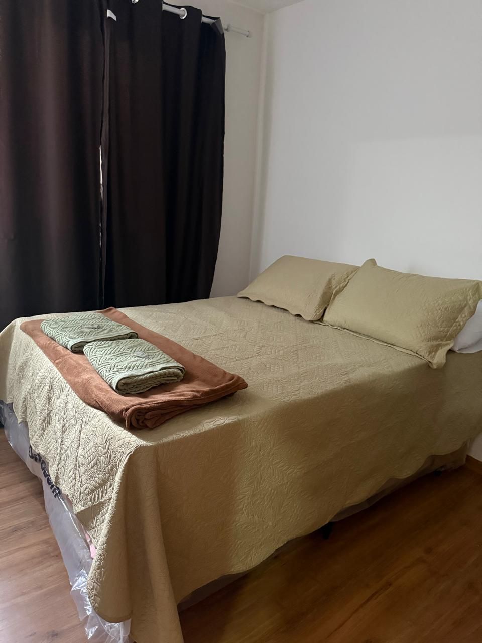 Una cama bien hecha con una colcha color beige y almohadas, una toalla doblada y una manta marrón al lado.