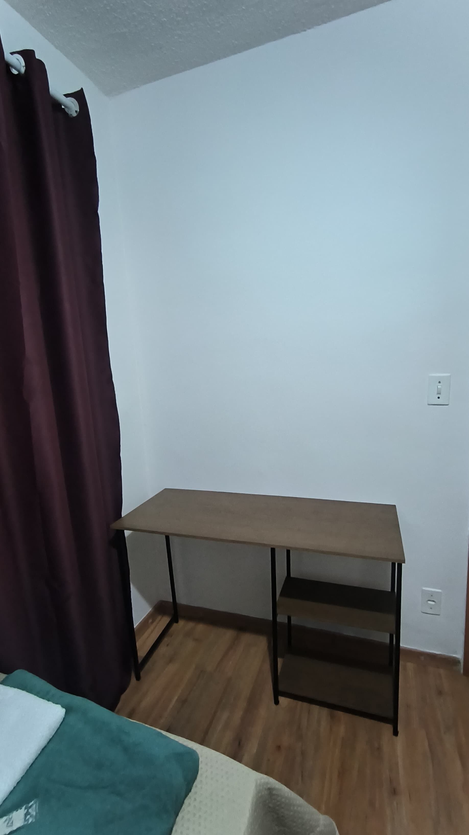 Une chambre avec un lit simple, un bureau et un rideau.