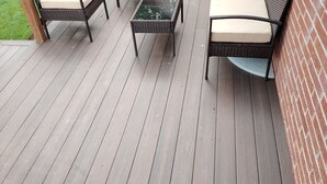 En træterrasse med udendørs møbler, heriblandt to fletstole og et lille bord.
