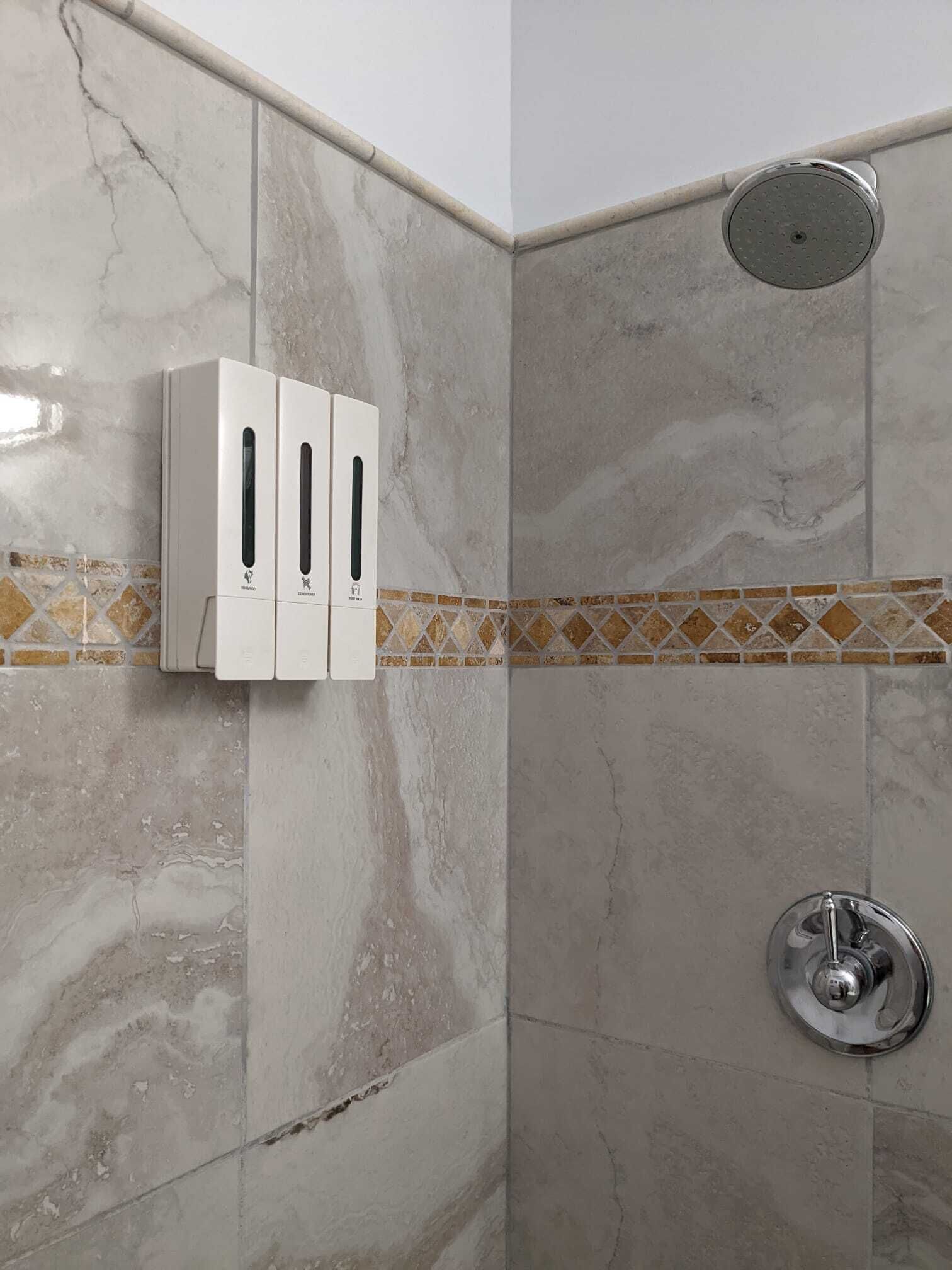 Ein Badezimmer mit Dusche, Handtuchspender und einer gefliesten Rückwand.