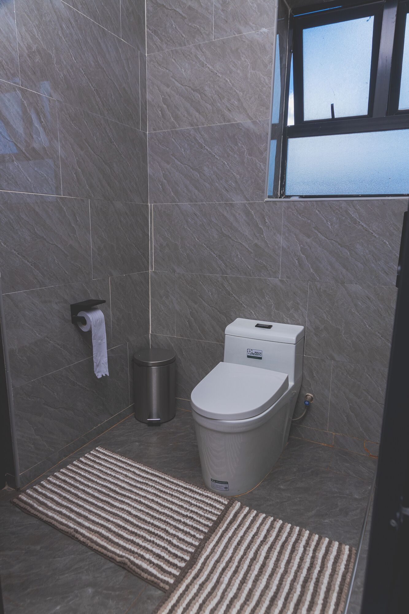 Un baño con inodoro, un cubo de basura y una ventana.
