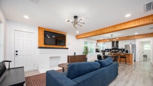 Ein modernes Wohnzimmer mit einem blauen Sofa, einem Kamin und einer Küchenzeile mit Holzbalken.