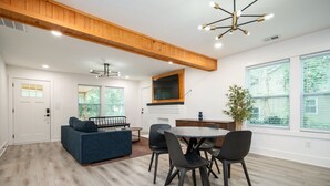 Ein modernes Wohnzimmer mit einem blauen Sofa, einem Esstisch mit Stühlen, einem Kamin und großen Fenstern.
