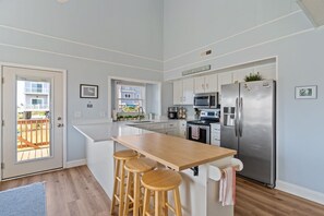A modern kitchen with a large island, stainless steel appliances, and a view to the outside.