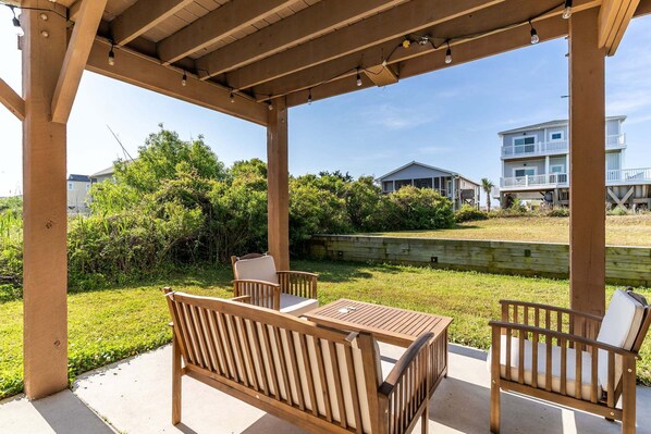 A covered patio with wooden furniture, a concrete floor, and a view of a house in the background.