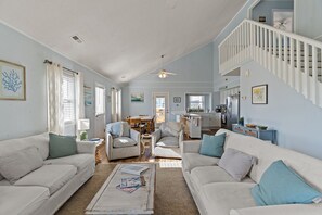 A spacious living area with a staircase, two sofas, striped chairs, and a dining table.