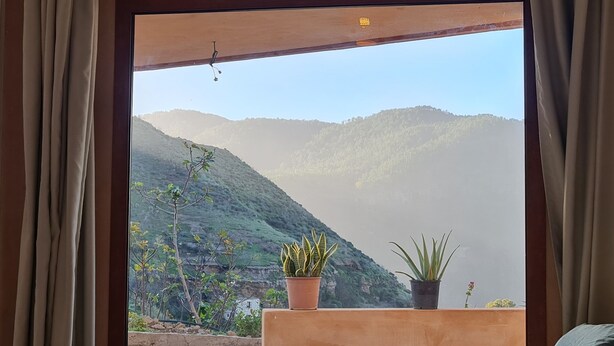 Ein Zimmer mit großem Fenster und Blick auf eine gebirgige Landschaft.