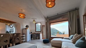 Ein modernes Wohnzimmer mit einer Couch, einem Essbereich und einer Küche. Ein großes Fenster bietet Blick ins Freie.