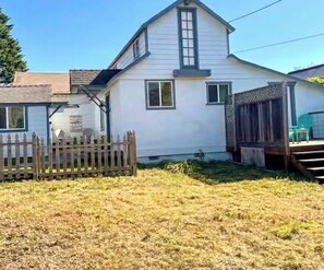 Une maison blanche d’un seul étage, dotée d’une cour clôturée, d’une terrasse en bois et d’un petit porche.