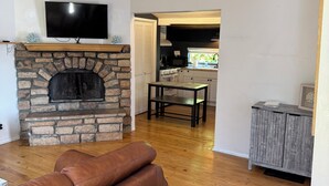 Ein Wohnzimmer mit Kamin aus Stein, einer Ledersofa und Holzboden, sowie einer Küche im Hintergrund.