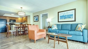 A modern living room with a blue sofa, orange armchair, and dining area with wooden chairs and a table.