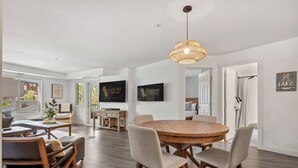 A spacious living room with a round wooden dining table, comfortable seating, and a large window offering a view of the outdoors. - La Bohème | Pool Views | Hot Tub | Lake Access (Invermere)